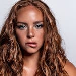 Studio headshot of a young woman with curly red hair on a white background.